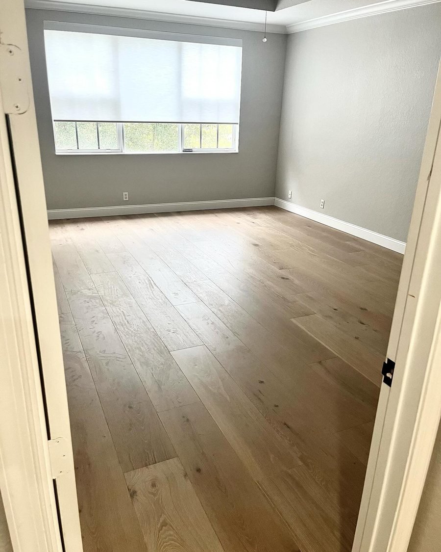 After: the same bedroom with light wide-plank flooring with natural knots and grain