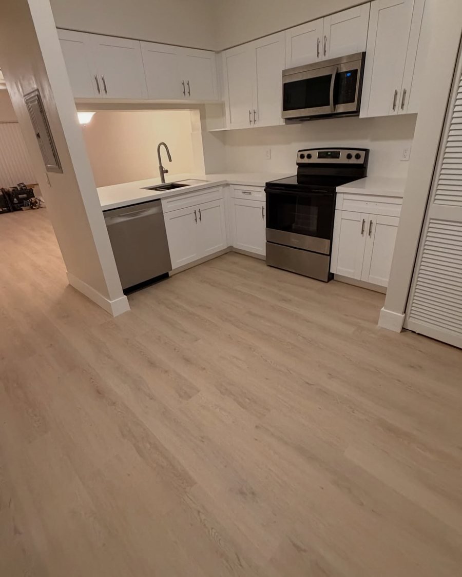 After: the same kitchen with white shaker cabinets, white countertops, a white backsplash, a workstation sink and a stainless dishwasher