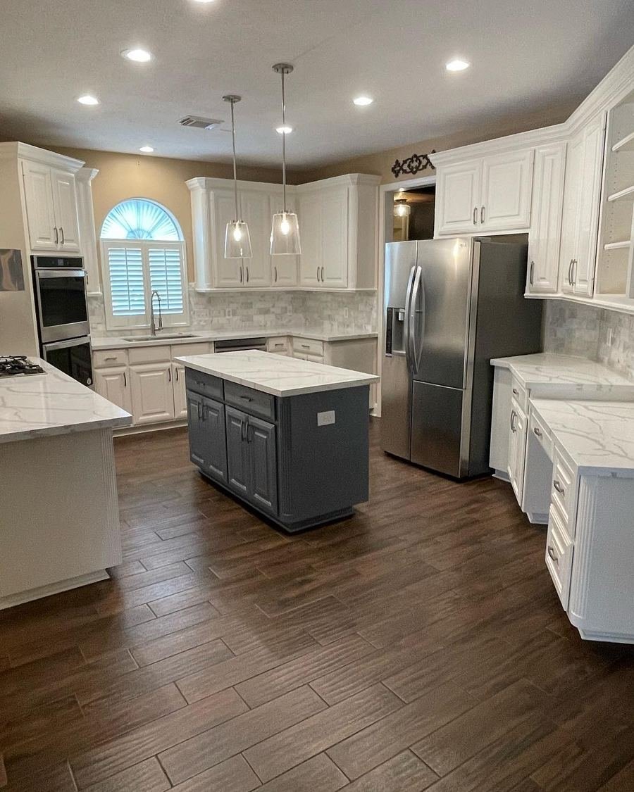 After: the same kitchen with dark wood-look plank tile, recessed lights, two glass pendants over the island and white veined countertops