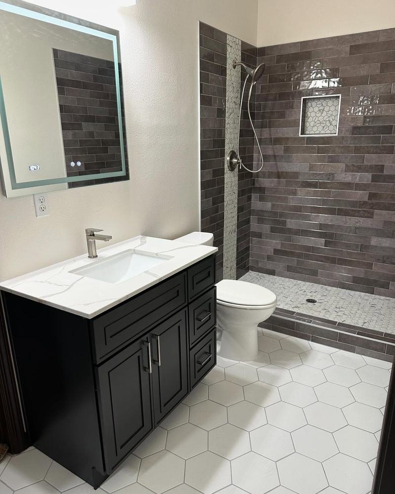Remodeled bathroom with a black shaker vanity, white hex floor tile and a dark tile shower accent