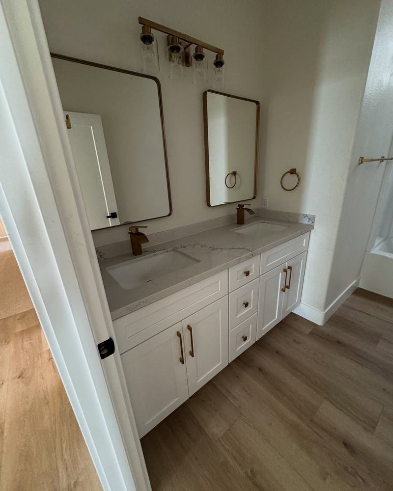 Remodeled bathroom with a white double vanity, gold faucets and black framed mirrors