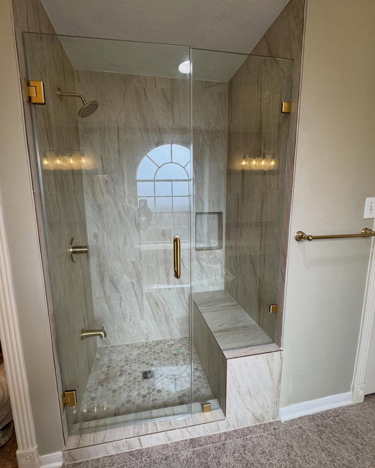 Finished walk-in shower with frameless glass, marble-look tile, a tiled bench and brushed gold fixtures
