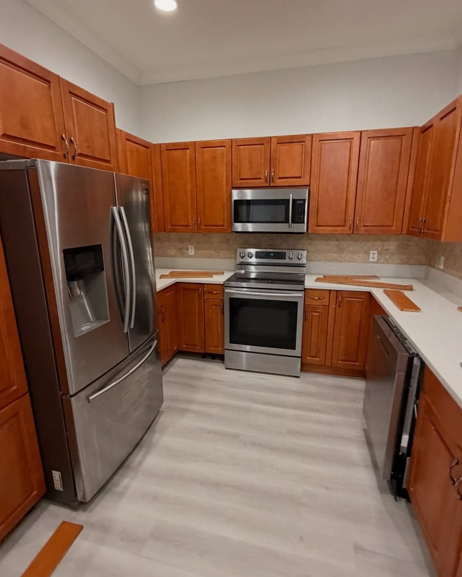 Before: kitchen with orange-toned wood cabinets, white countertops and gray plank floors