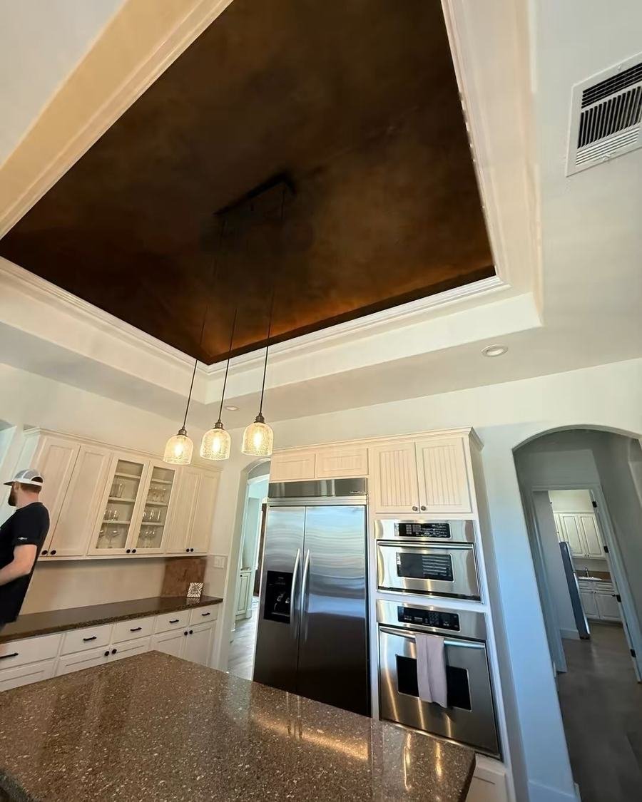 Before: kitchen with a dark painted tray ceiling, three small pendant lights and a speckled brown countertop on the island
