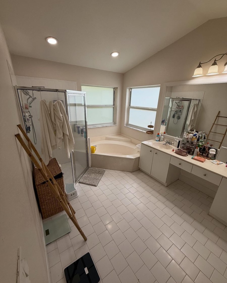 Before: primary bathroom with a corner garden tub, a framed glass shower stall, white floor tile and an older white vanity