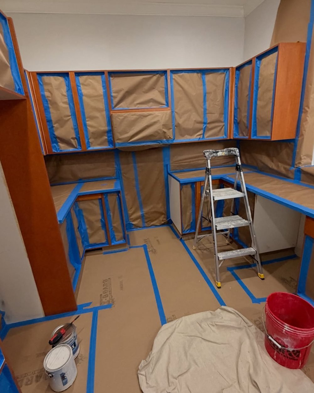 Kitchen masked off with brown paper and blue tape before cabinet painting