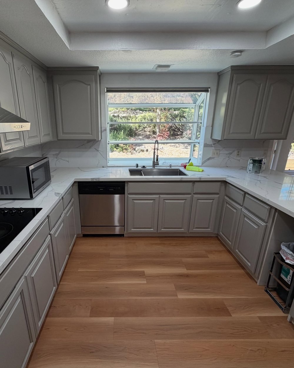 U-shaped kitchen with gray painted cabinets, marble-look counters and a garden window