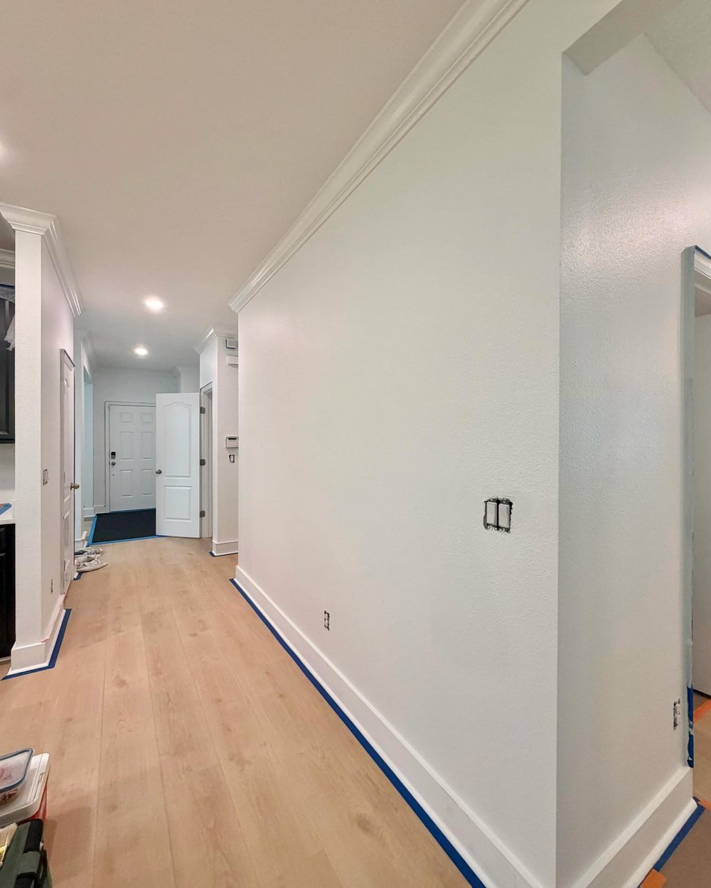 Hallway with fresh white walls and crown molding, with painter's tape still on the baseboards