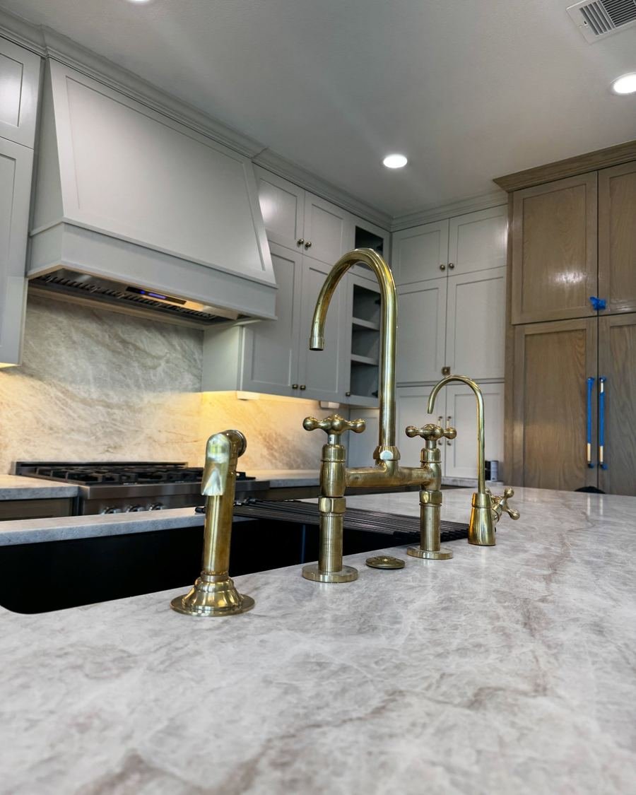 White and gray veined kitchen countertop with an undermount sink and a brass bridge faucet