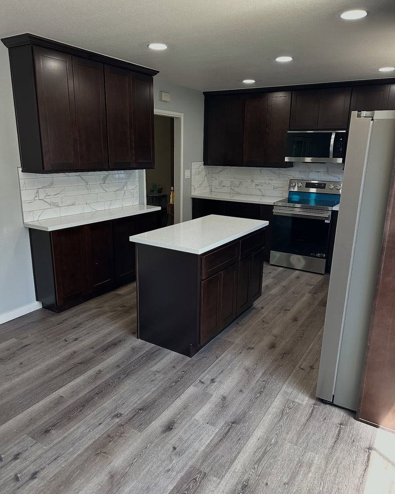 Kitchen with espresso shaker cabinets, a white quartz island and light gray plank floors