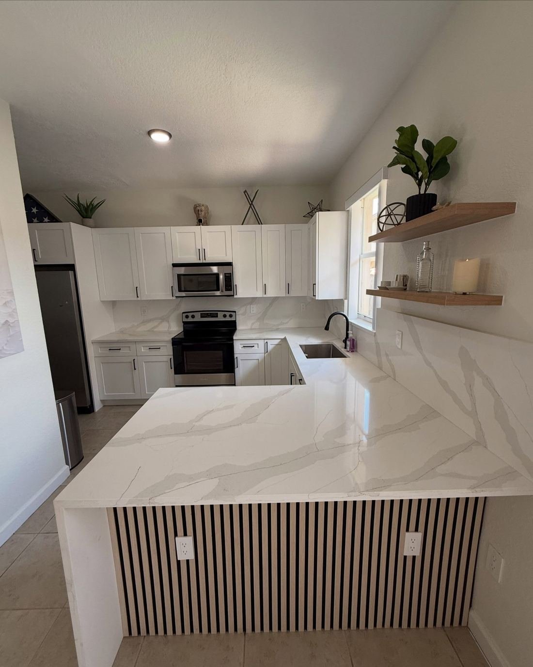 Kitchen island with a white veined waterfall countertop and a vertical slat panel