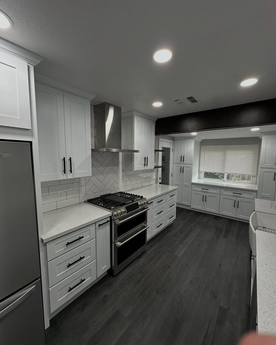 Kitchen with white shaker cabinets, a stainless range hood, dark wood-look floors and black hardware