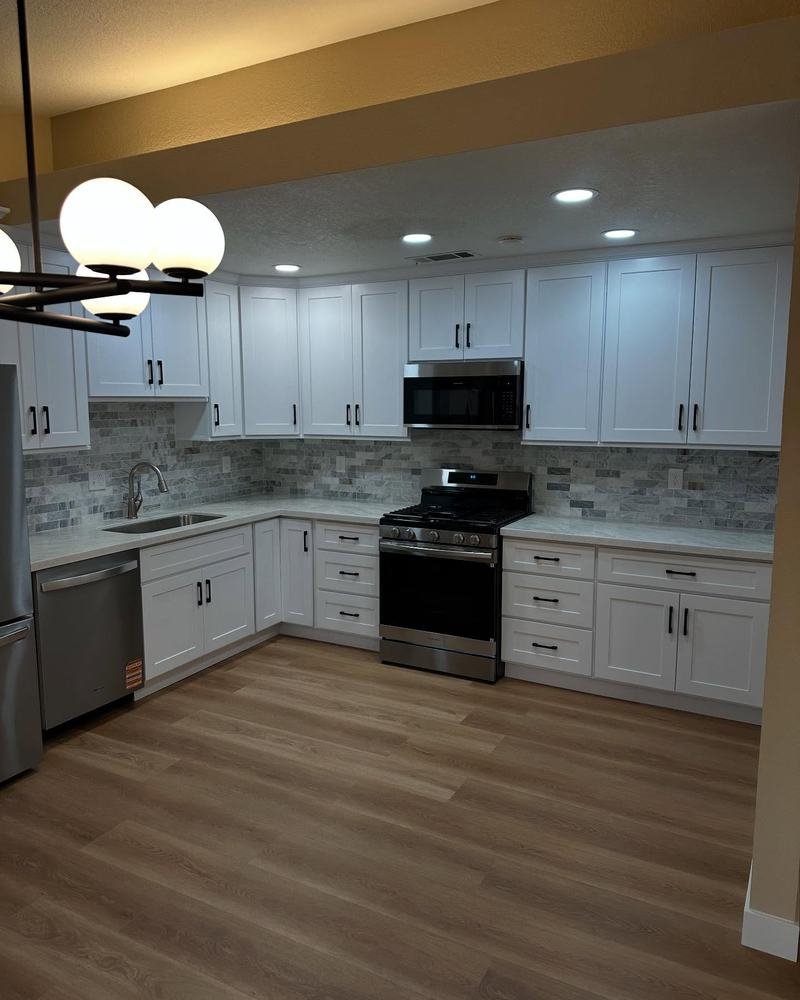 Kitchen with white shaker cabinets, stainless appliances, a glass globe chandelier and wood-look floors