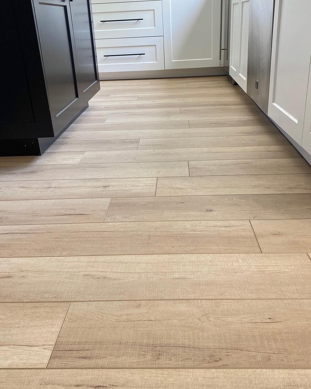 Light wood-look plank flooring in a kitchen with a black island and white cabinets