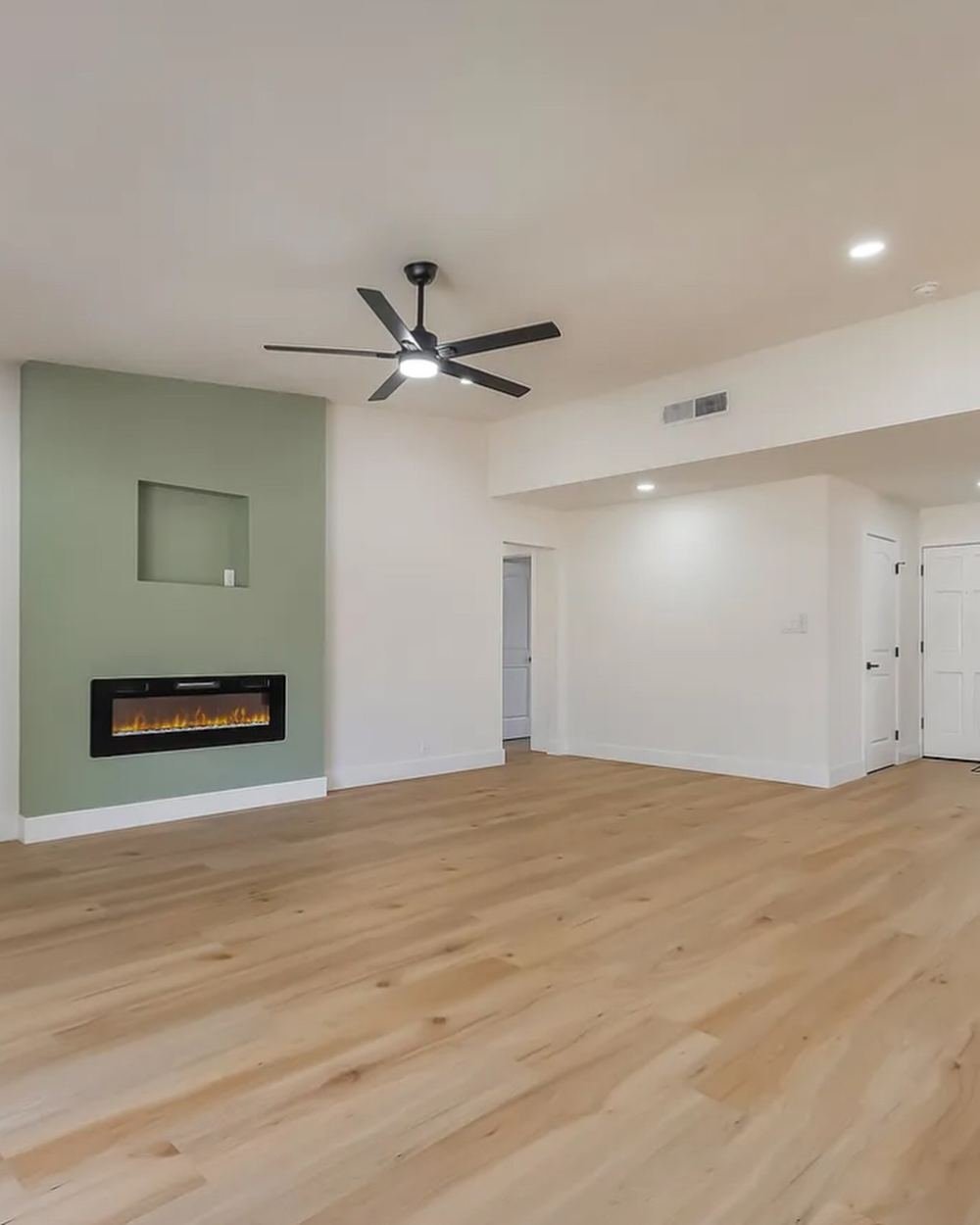 Living room with light wood-look flooring, a sage green accent wall and a built-in electric fireplace