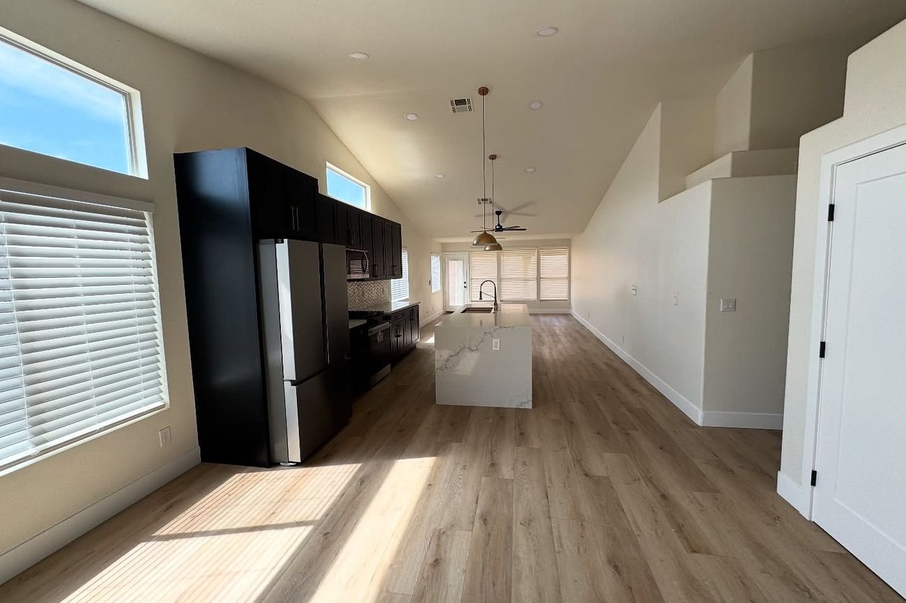 Open-concept kitchen and living area after remodel with dark cabinets, a white island and continuous wood-look flooring