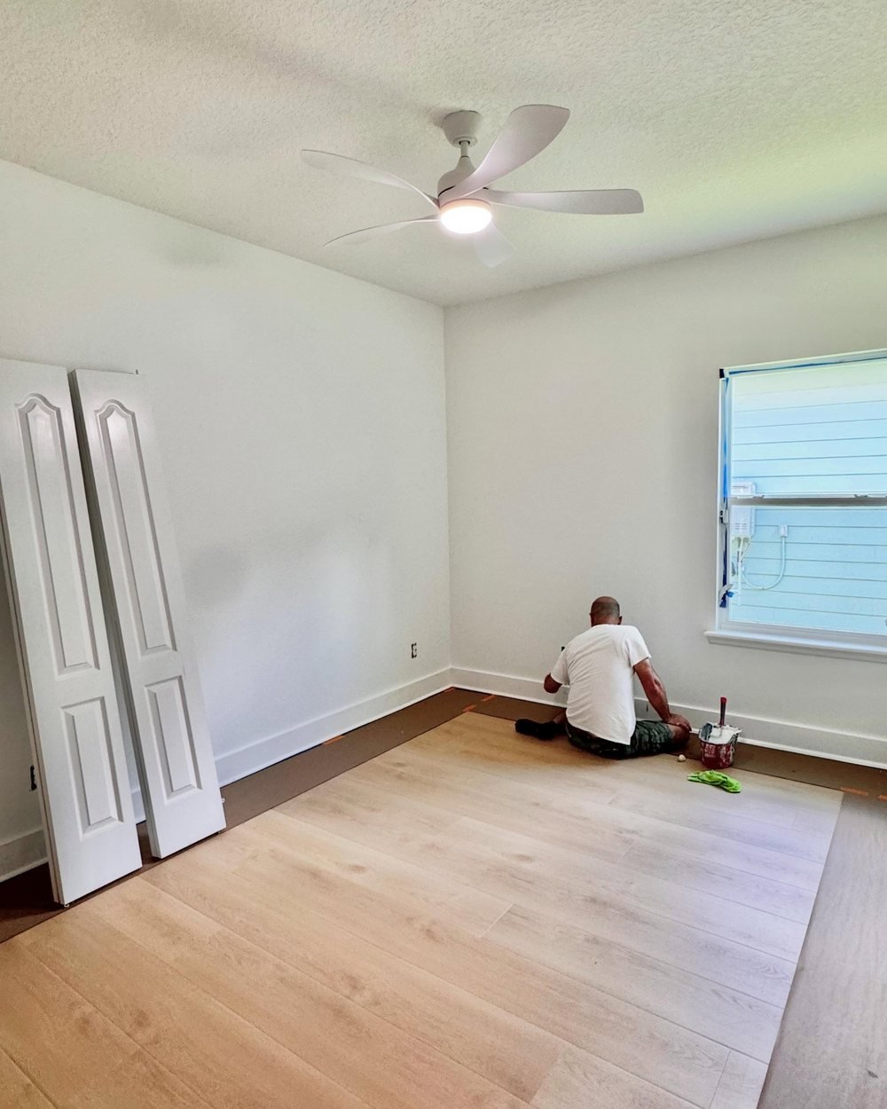 Painter cutting in white baseboards in a bedroom with the floor protected