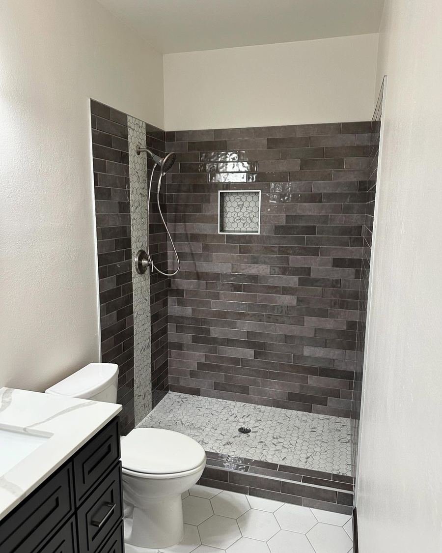 Walk-in shower with dark gray brick-pattern tile, a mosaic accent strip, a niche and a pebble floor