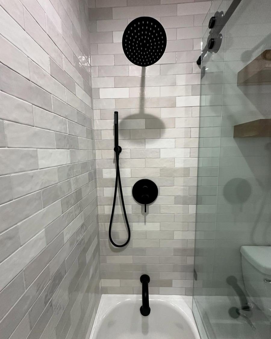Tub-shower with gray subway-style tile, a matte black rain head, handheld sprayer and sliding glass door