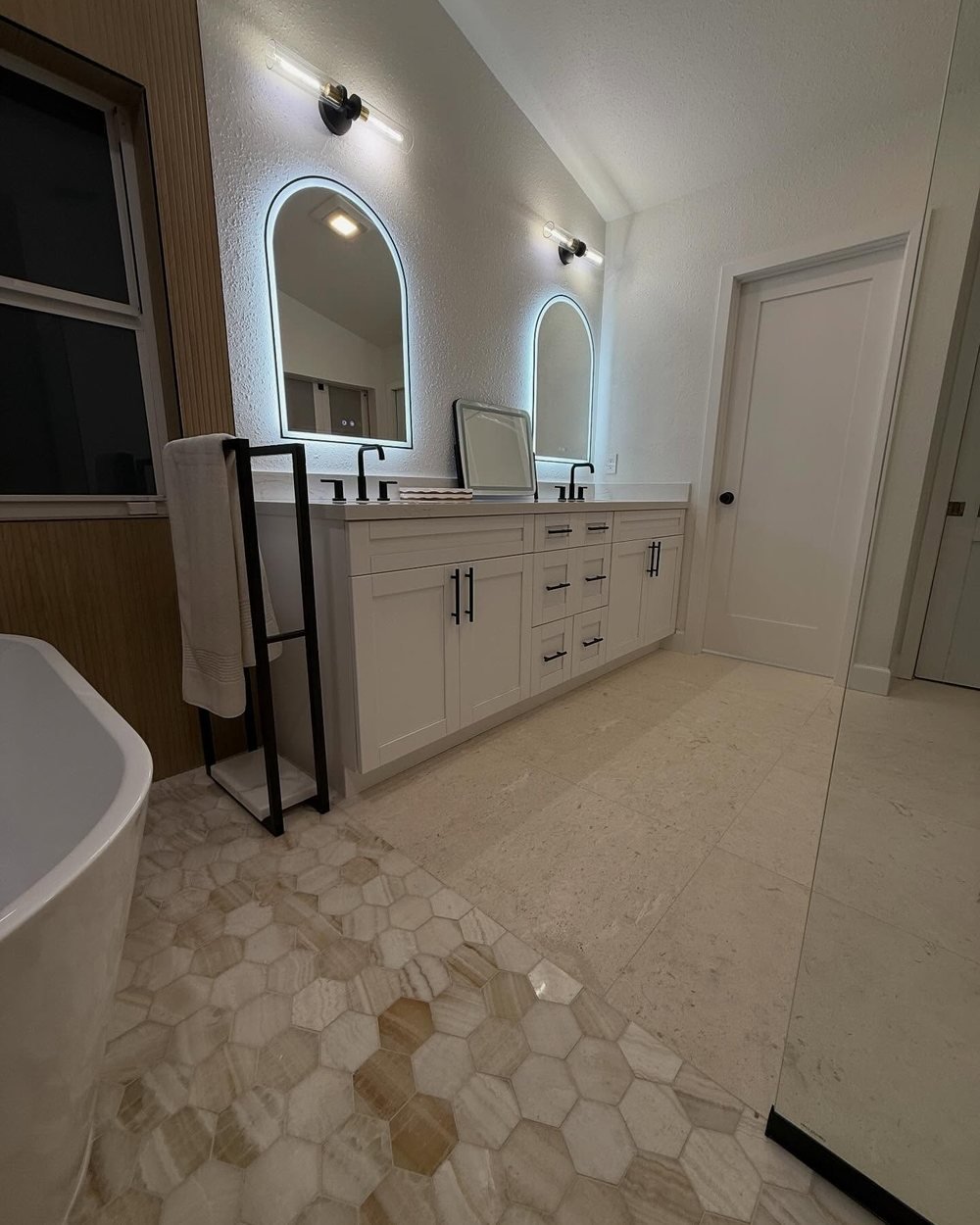 Double vanity next to a freestanding tub, with a hexagon mosaic floor meeting large-format floor tile