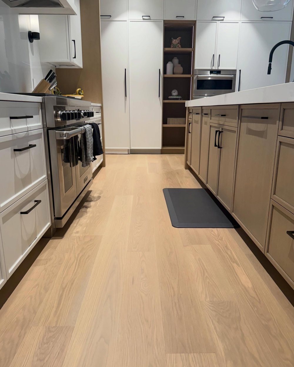 Light wide-plank wood floor down a kitchen aisle between white and oak cabinets