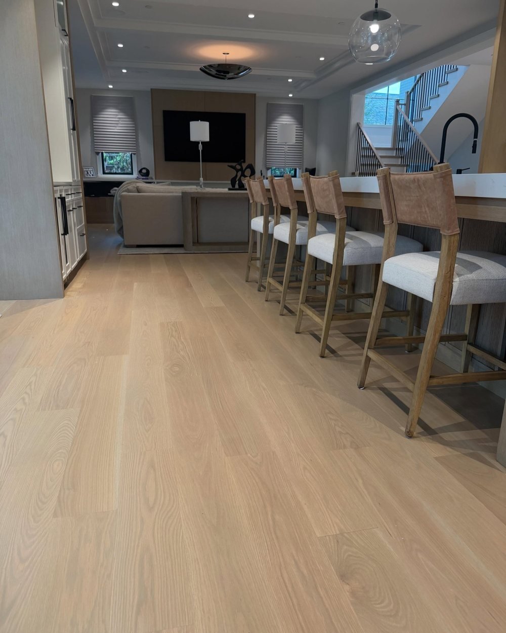 Light wide-plank wood floor running along a kitchen island into the living room